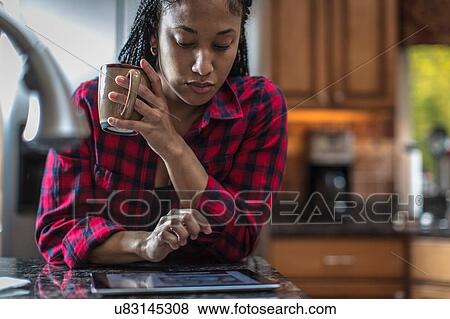 Mid adult woman at kitchen counter reading digital tablet View Large Photo Image Stock Photo - Mid adult woman at kitchen counter reading digital tablet. Fotosearch