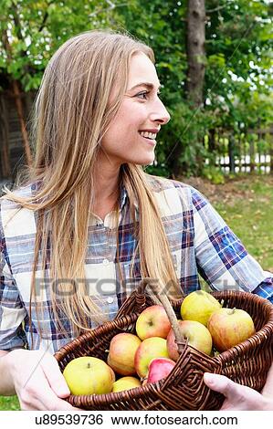 Stock Photograph - Mid adult woman holding basket of homegrown apples. Fotosearch