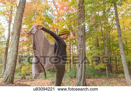 Stock Image - Mid adult woman holding up her shawl in autumn forest. Fotosearch