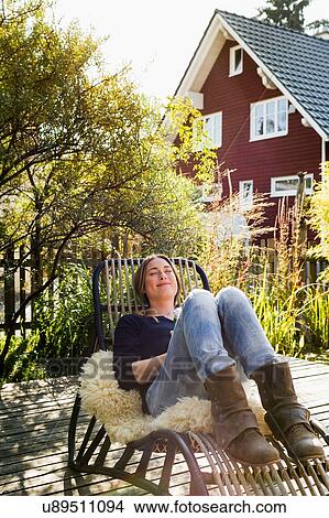 Mid adult woman relaxing on lounge chair on wooden decking View Large Photo Image Picture - Mid adult woman relaxing on lounge chair on wooden decking. Fotosearch