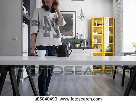Mid adult woman wearing headphones around her neck at kitchen table View Large Photo Image Stock Image - Mid adult woman wearing headphones around her neck at kitchen table. Fotosearch