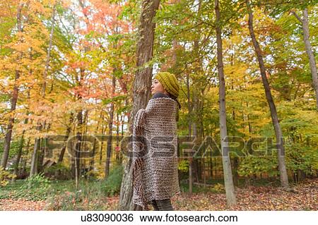 Stock Photograph - Mid adult woman wrapped in shawl standing in autumn forest. Fotosearch