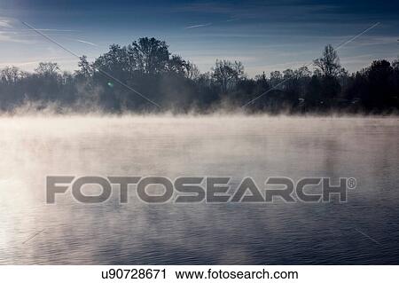 Stock Image - Misty lake with trees in background. Fotosearch