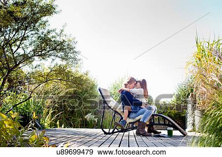 Stock Photo - Mother and daughter hugging on lounge chair on decking. Fotosearch