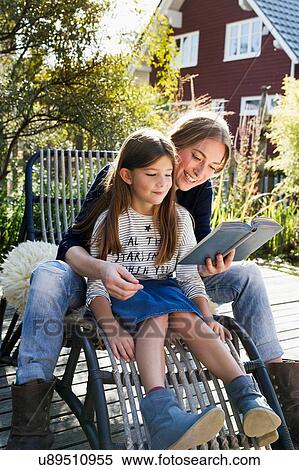 Stock Photography - Mother and daughter sitting on chair outdoors reading book. Fotosearch