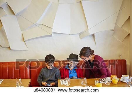 Stock Photo - Mother and sons using digital tablet and smartphone in restaurant. Fotosearch