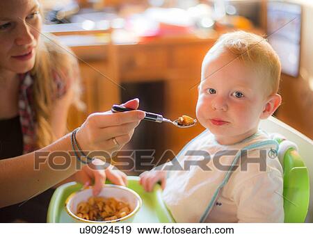 Mother feeding her toddler in a high chai View Large Photo Image Stock Photo - Mother feeding her toddler in a high chai. Fotosearch
