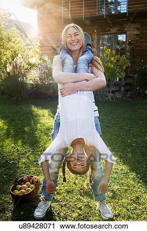 Stock Image - Mother lifting daughter upside down in garden. Fotosearch