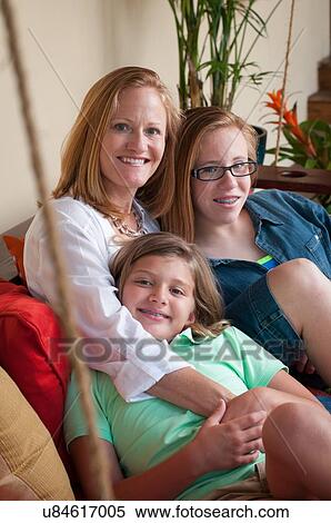 Stock Photography - Mother sitting with daughters looking at camera smiling. Fotosearch