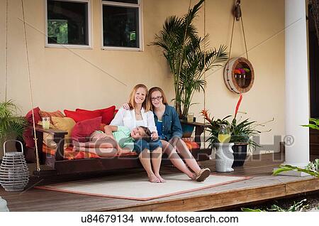 "Mother with daughters, sitting on porch swing looking at camera smiling" View Large Photo Image Picture - "Mother with daughters, sitting on porch swing looking at camera smiling". Fotosearch