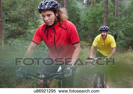 Stock Photography - Mountain biking couple biking through forest. Fotosearch