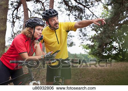 Stock Photograph - Mountain biking couple using smartphone navigation in forest. Fotosearch