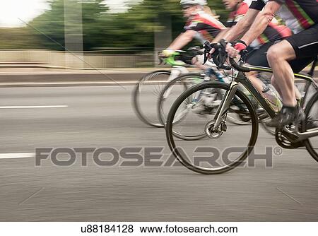 Neck down view of three cyclists speeding on urban road in racing cycle race View Large Photo Image Stock Photo - Neck down view of three cyclists speeding on urban road in racing cycle race. Fotosearch