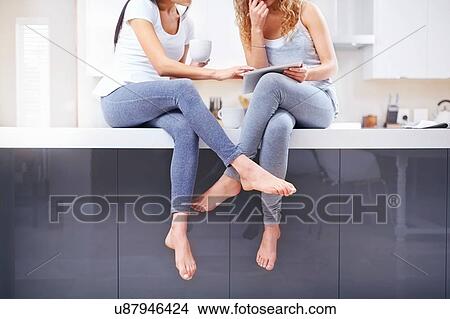 Neck down view of two young women using digital tablet at kitchen counter View Large Photo Image Picture - Neck down view of two young women using digital tablet at kitchen counter. Fotosearch