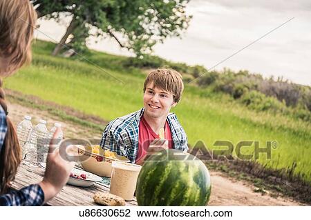 Over shoulder view of young woman and man chatting at picnic table View Large Photo Image Stock Image - Over shoulder view of young woman and man chatting at picnic table. Fotosearch