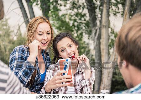 Stock Photo - Over shoulder view of young women eating cherries taking smartphone selfie. Fotosearch