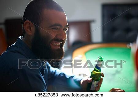 Stock Image - Over the shoulder view of men drinking beer at pub card table. Fotosearch
