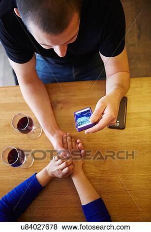 Stock Photo - Overhead cropped view of man holding girlfriends hand whilst reading smartphone in restaurant. Fotosearch