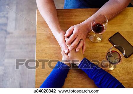 Stock Image - Overhead cropped view of romantic couple holding hands in restaurant. Fotosearch
