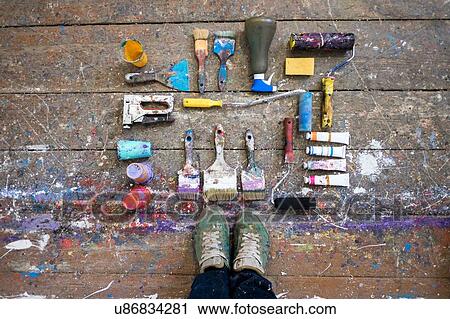 Stock Image - Overhead view of artists feet and art equipment on paint splashed floorboard. Fotosearch