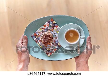 Stock Photo - Overhead view of female hands holding plate of dessert and cup of espresso. Fotosearch