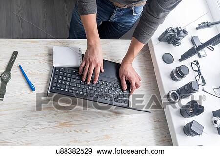 Stock Photo - Overhead view of male photographer typing on studio desk laptop. Fotosearch