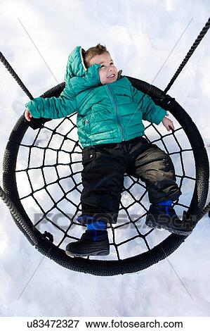 Stock Photo - Overhead view of preschool boy lying on hammock swing in snow looking away smiling. Fotosearch