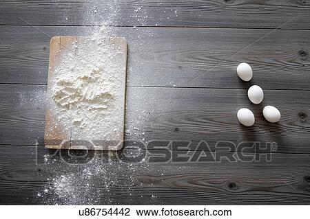 Stock Image - Overhead view of raw eggs and flour on kitchen table. Fotosearch