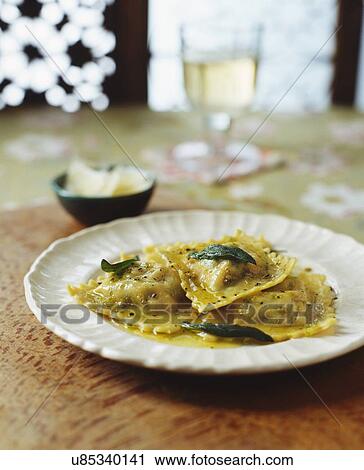 Stock Image - Plate of ravioli with italian sausage meat, butter, pepper, herbs and parmesan, white wine. Fotosearch