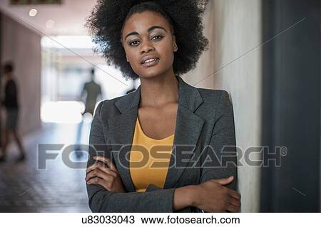 Portrait of confident young businesswomen leaning against office wall View Large Photo Image Stock Image - Portrait of confident young businesswomen leaning against office wall. Fotosearch