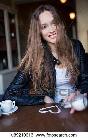 Stock Image - Portrait of happy mid adult woman pouring sugar heart on cafe table. Fotosearch