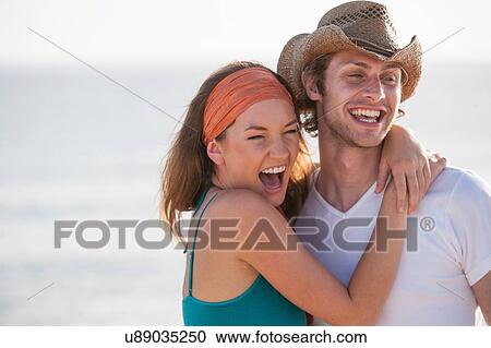 Stock Image - Portrait of happy young couple hugging at seaside. Fotosearch