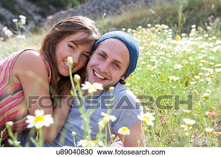 Stock Image - Portrait of happy young couple reclining in field of wild flowers. Fotosearch