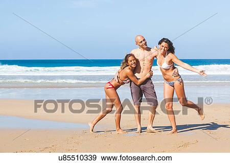 Stock Photo - Portrait of man and two young women wearing swimwear on beach, El Cotillo, Fuerteventura, Spain. Fotosearch