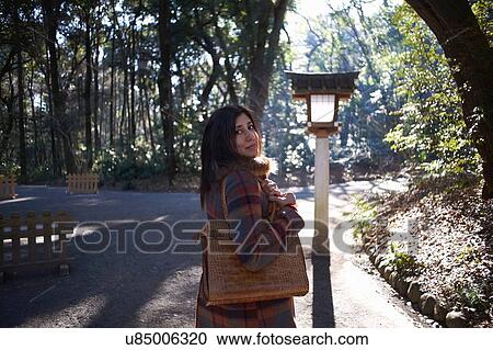 Stock Image - Portrait of mature female tourist looking over her shoulder in park, Tokyo, Japan. Fotosearch