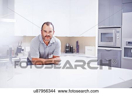 Picture - Portrait of mature man leaning on kitchen counter. Fotosearch