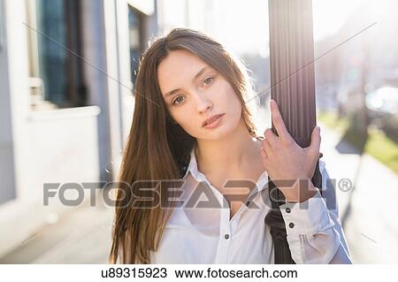 Stock Image - Portrait of mid adult woman holding street lamp post. Fotosearch