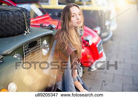 Stock Photo - Portrait of mid adult woman sitting against parked vintage four wheel drive. Fotosearch