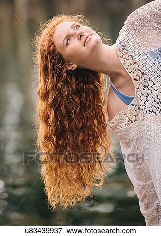 Stock Photo - Portrait of serene young woman with long red hair gazing from river. Fotosearch
