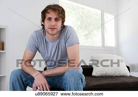 Stock Photo - Portrait of serious young man on living room sofa. Fotosearch