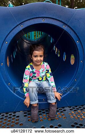 Stock Image - Portrait of shy girl sitting in playground tunnel. Fotosearch