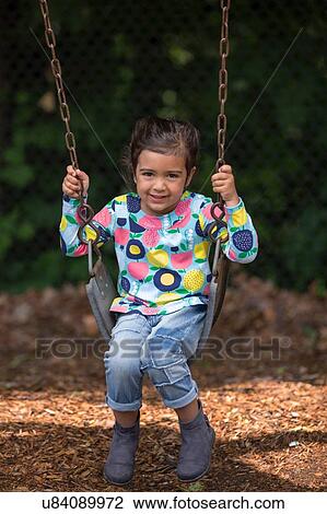 Stock Image - Portrait of shy girl swinging on playground swing. Fotosearch