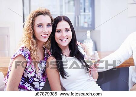 Stock Photography - Portrait of two female friends drinking wine in kitchen. Fotosearch