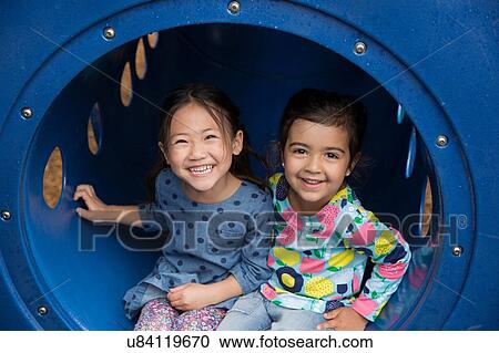 Stock Image - Portrait of two girls sitting in playground tunnel. Fotosearch