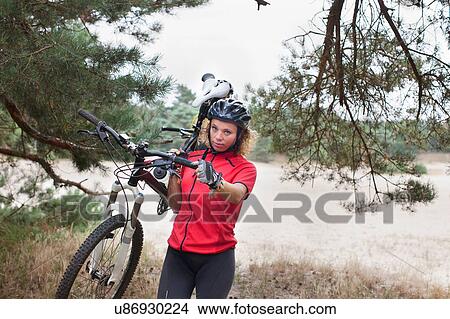 Portrait of woman mountain biker carrying cycle over sand on riverbank View Large Photo Image Picture - Portrait of woman mountain biker carrying cycle over sand on riverbank. Fotosearch