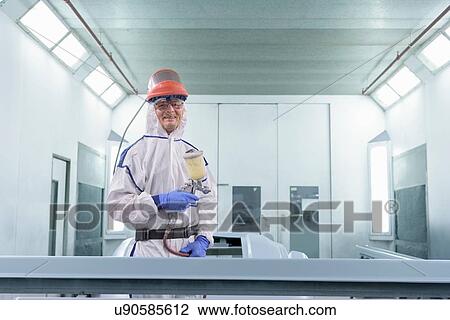 Stock Image - Portrait of worker paint spraying parts on automotive production line. Fotosearch