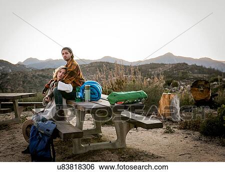 "Portrait of young couple sitting on picnic bench in rural setting, young man sitting behind young woman" View Large Photo Image Stock Photograph - "Portrait of young couple sitting on picnic bench in rural setting, young man sitting behind young woman". Fotosearch