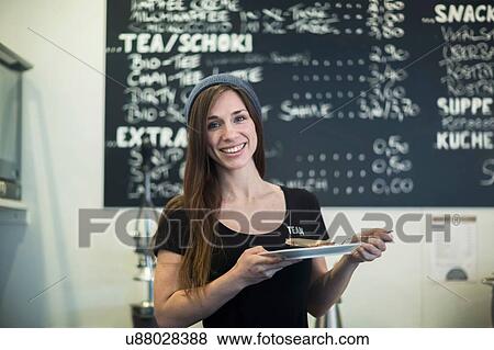 Stock Photo - Portrait of young female waitress holding plate and cake slice in cafe. Fotosearch