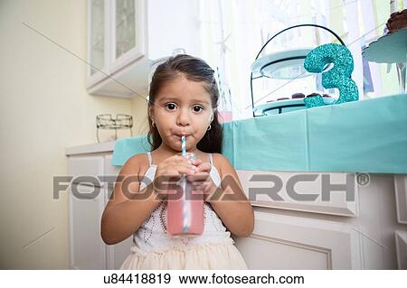 Stock Photo - Portrait of young girl drinking drink through straw at birthday party. Fotosearch