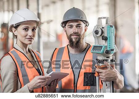 Stock Image - Portrait of young male and female surveyors on construction site. Fotosearch